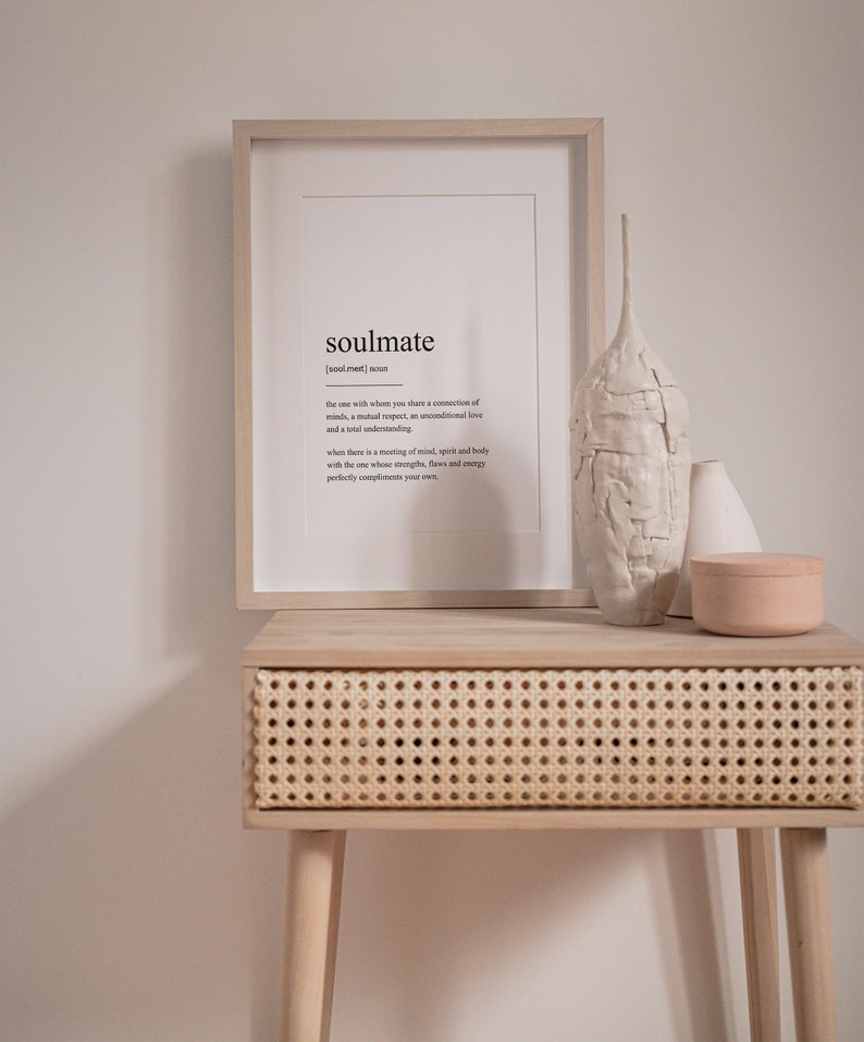 Peut inclure: Une impression encadr&eacute;e avec la d&eacute;finition du mot "&acirc;me s&oelig;ur" en texte noir sur fond blanc. L'impression est pos&eacute;e sur une table en bois clair avec un tiroir en rotin tiss&eacute;. Il y a deux vases en c&eacute;ramique blanche et un r&eacute;cipient en c&eacute;ramique rose sur la table.