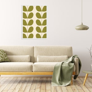 May include: A framed print of a green and white abstract pattern with leaf shapes. The print is hanging on a white wall above a beige sofa with a green throw blanket.