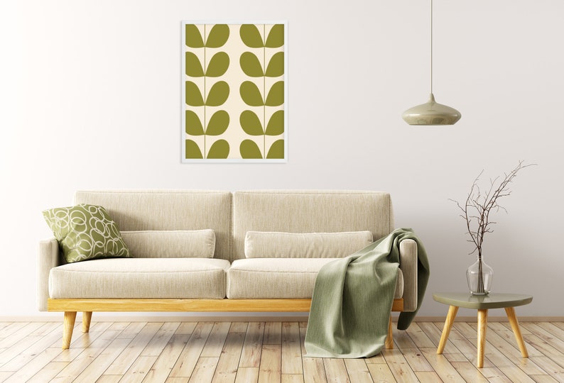 May include: A framed print of a green and white abstract pattern with leaf shapes. The print is hanging on a white wall above a beige sofa with a green throw blanket.