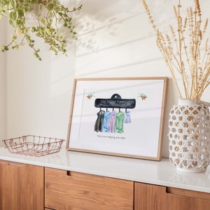 May include: A watercolor illustration of a chalkboard sign that reads "The Doyle Family" with five coats hanging on hooks. The text below the sign reads "This is our happily ever after".