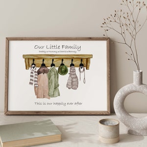 May include: A watercolor illustration of a wooden coat rack with four hooks. There are four items hanging on the hooks: a scarf, a jacket, a hat, and another scarf. The text "Our Little Family" is above the coat rack, and the text "Daddy Mummy Charlie Barney" is below the coat rack. The text "This is our happily ever after" is below the coat rack.