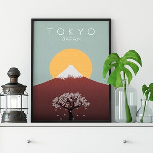 Puede incluir: Un p&oacute;ster minimalista con un dise&ntilde;o gr&aacute;fico del Monte Fuji, un &aacute;rbol de cerezo en flor y un sol amarillo. El p&oacute;ster tiene el texto "TOKYO JAP&Oacute;N" en la parte superior.
