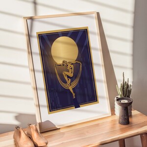 May include: A gold framed print with a gold silhouette of a dancer against a dark blue background with a large gold moon in the upper center of the image.