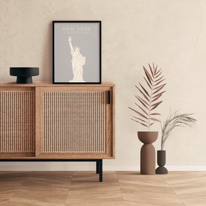 May include: A wooden cabinet with two sliding doors, a black top, and a framed print of the Statue of Liberty with the text "NEW YORK, UNITED STATES OF AMERICA".
