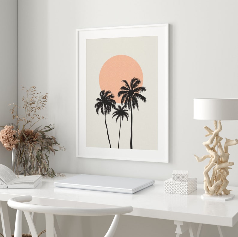 May include: A framed print with a minimalist design featuring three palm trees silhouetted against a peach-colored sun on a beige background.