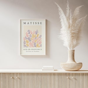 May include: A framed print of a Matisse painting featuring a colorful abstract design of leaves in pink, purple, and yellow. The print is titled "Aix-en-Provence, Pavillon de Vend&ocirc;me" and is displayed on a white wall above a wooden cabinet.