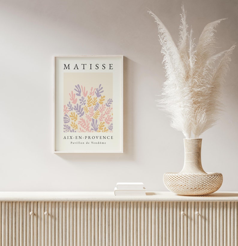 May include: A framed print of a Matisse painting featuring a colorful abstract design of leaves in pink, purple, and yellow. The print is titled "Aix-en-Provence, Pavillon de Vend&ocirc;me" and is displayed on a white wall above a wooden cabinet.