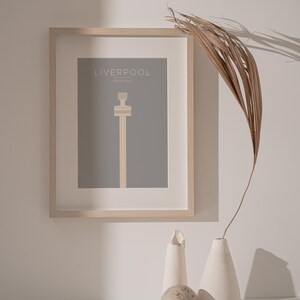 May include: A framed print of a minimalist illustration of the Liver Building in Liverpool, England. The print is on a gray background with the text "LIVERPOOL" and "ENGLAND" in white.