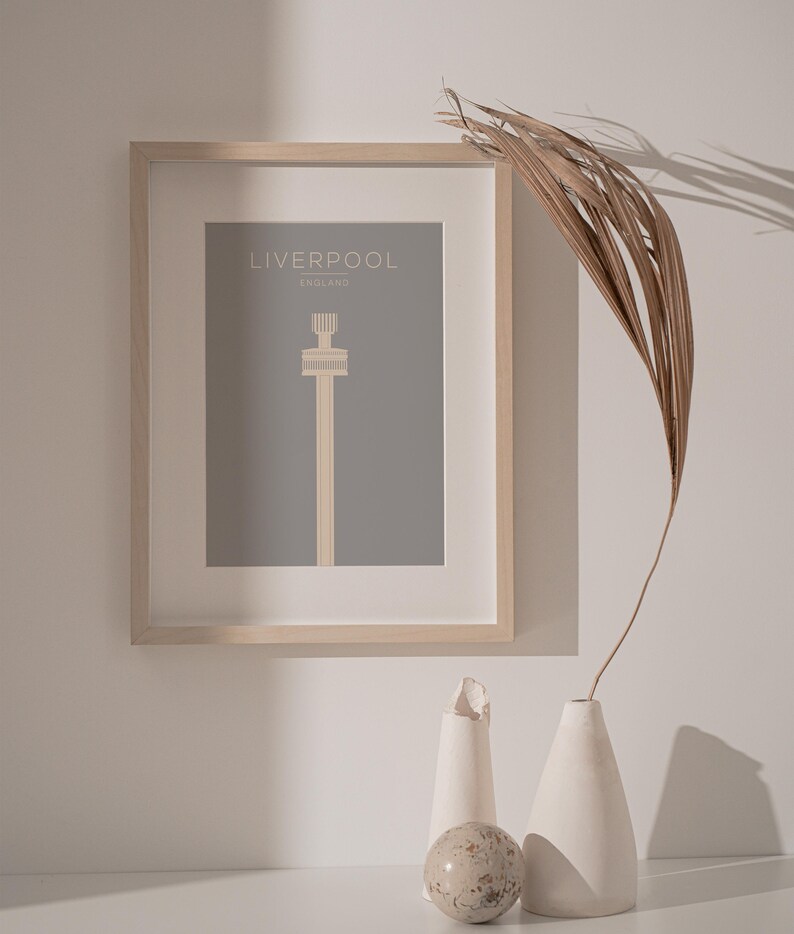 May include: A framed print of a minimalist illustration of the Liver Building in Liverpool, England. The print is on a gray background with the text "LIVERPOOL" and "ENGLAND" in white.