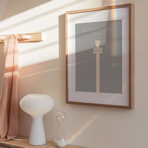 May include: A framed print with a minimalist design of the Liver Building in Liverpool, England. The print is on a gray background with the text "Liverpool, England" in white.