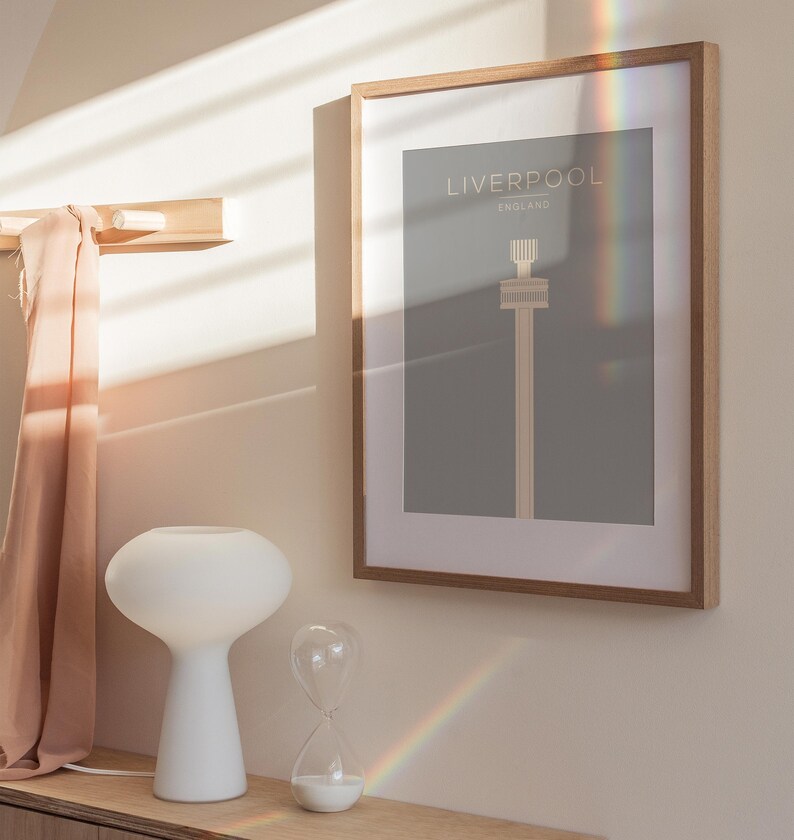 May include: A framed print with a minimalist design of the Liver Building in Liverpool, England. The print is on a gray background with the text "Liverpool, England" in white.