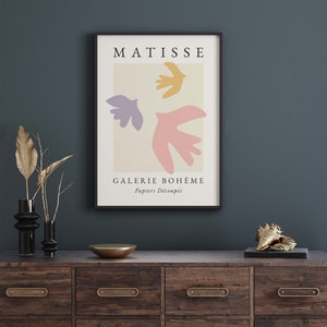 May include: A black framed poster with a beige background featuring a Matisse art print of three colorful paper cutouts of birds. The text "MATISSE" is at the top of the poster and "GALERIE BOHEME Papiers Decoup&eacute;s" is at the bottom.