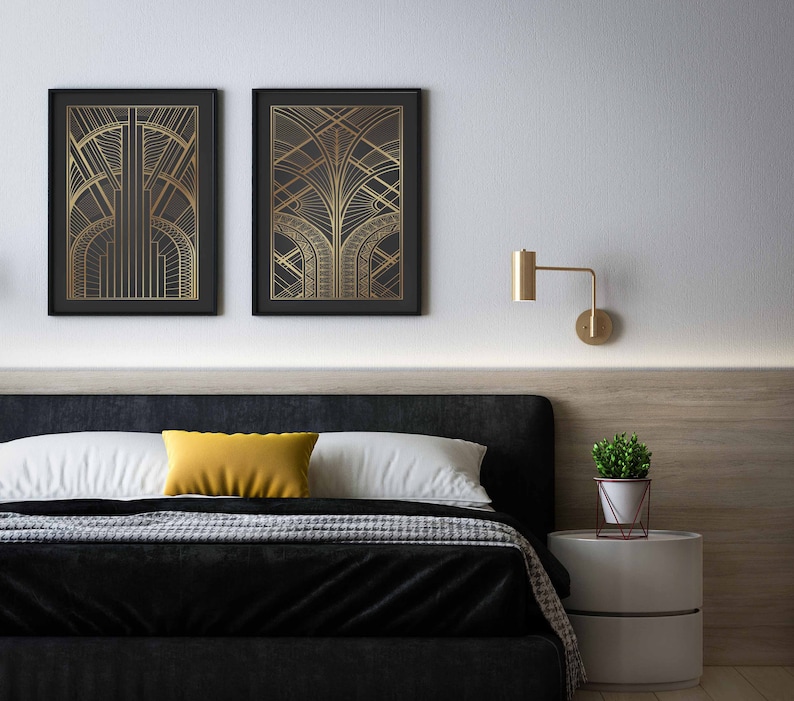 May include: A black bed frame with a white headboard and a black and white patterned blanket. There are two gold framed prints with geometric designs above the bed. A small plant in a white pot sits on a white nightstand.