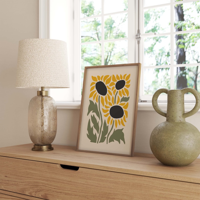 May include: A framed print of a stylized sunflower design with three sunflowers in shades of yellow and green on a cream background.