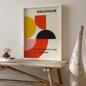 May include: A framed poster with a geometric design in red, yellow, black, and pink. The poster reads "BAUHAUS" and "ENTWIRF AUSSTELLUNG JULI - OKTOBER".