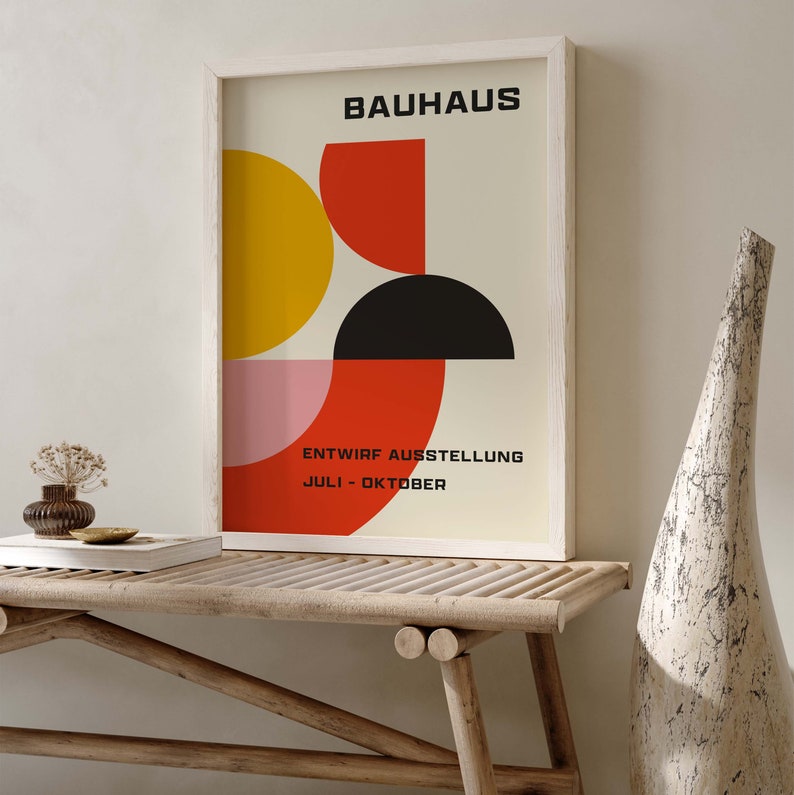 May include: A framed poster with a geometric design in red, yellow, black, and pink. The poster reads "BAUHAUS" and "ENTWIRF AUSSTELLUNG JULI - OKTOBER".
