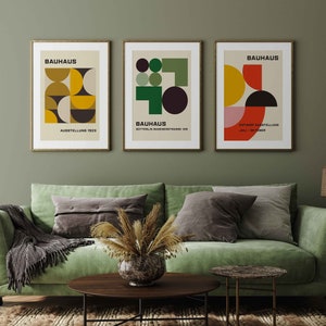May include: Three framed prints with geometric designs in shades of yellow, green, red, and black. The prints are titled "Bauhaus" and feature the text "Ausstellung 1923", "Sommerlin Badensstrasse 109", and "Entwurf Ausstellung Juli - Oktober".