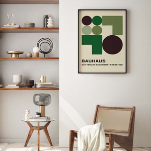 May include: A black framed poster with a geometric design in shades of green and brown. The poster has the text "BAUHAUS" and "S&Uuml;TTERLIN BADENSTRASSE 109" printed on it.