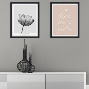 Puede incluir: Dos impresiones enmarcadas en una pared gris. La impresi&oacute;n de la izquierda es una ilustraci&oacute;n en blanco y negro de un loto indio. La impresi&oacute;n de la derecha es un fondo rosa claro con las palabras francesas "Un deux trois quatre" escritas en cursiva blanca.