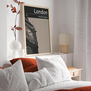 Peut inclure: Une affiche en noir et blanc encadr&eacute;e avec une photo du Big Ben &agrave; Londres, en Angleterre. L'affiche porte le texte "London" et "United Kingdom". L'affiche est accroch&eacute;e &agrave; un mur blanc au-dessus d'un lit avec une literie blanche et rouge.