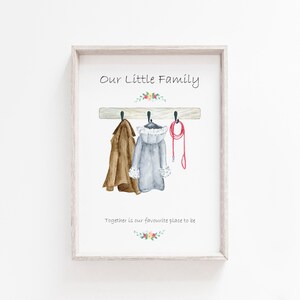 May include: A watercolor illustration of a wooden coat rack with two coats and a leash hanging on it. The text "Our Little Family" is above the rack and "Together is our favourite place to be" is below the rack.