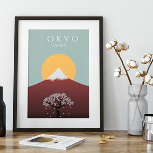 Puede incluir: Una impresi&oacute;n enmarcada con un dise&ntilde;o minimalista que presenta el Monte Fuji, un &aacute;rbol de cerezo en flor y un sol amarillo sobre un fondo azul y rojo. El texto "TOKYO JAP&Oacute;N" est&aacute; en la parte superior de la impresi&oacute;n.