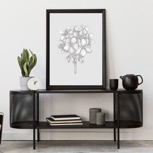 May include: A black metal console table with two shelves. The top shelf has a black framed print of a gray floral illustration. The bottom shelf has a stack of books and two gray cylindrical containers.