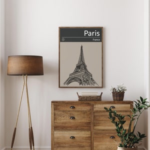 Peut inclure: Une illustration en noir et blanc de la tour Eiffel &agrave; Paris, en France. L'illustration est encadr&eacute;e dans un cadre en bois brun et est accroch&eacute;e &agrave; un mur blanc au-dessus d'une commode en bois.