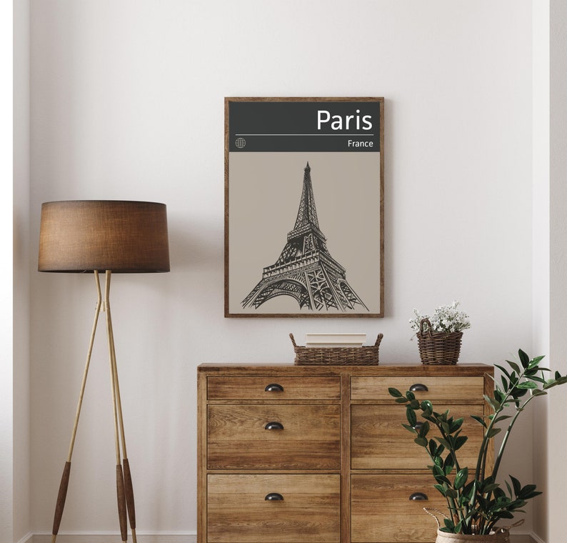 Peut inclure: Une illustration en noir et blanc de la tour Eiffel &agrave; Paris, en France. L'illustration est encadr&eacute;e dans un cadre en bois brun et est accroch&eacute;e &agrave; un mur blanc au-dessus d'une commode en bois.