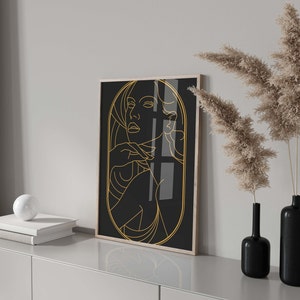 May include: A black and gold framed print of a line drawing of a woman's face and shoulders. The woman is looking to the side and has her hand on her chin.