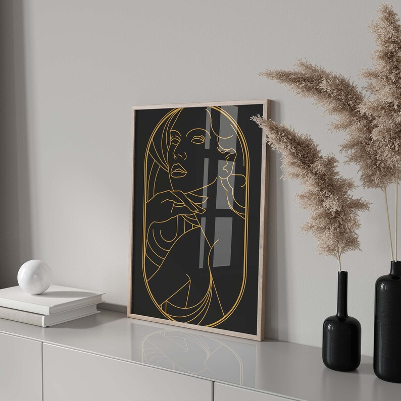 May include: A black and gold framed print of a line drawing of a woman's face and shoulders. The woman is looking to the side and has her hand on her chin.
