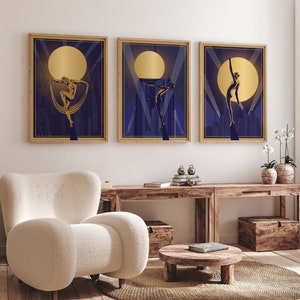 May include: Three framed art prints with a gold and blue color scheme. Each print features a silhouette of a woman in a stylized pose against a backdrop of a city skyline and a large, golden moon.