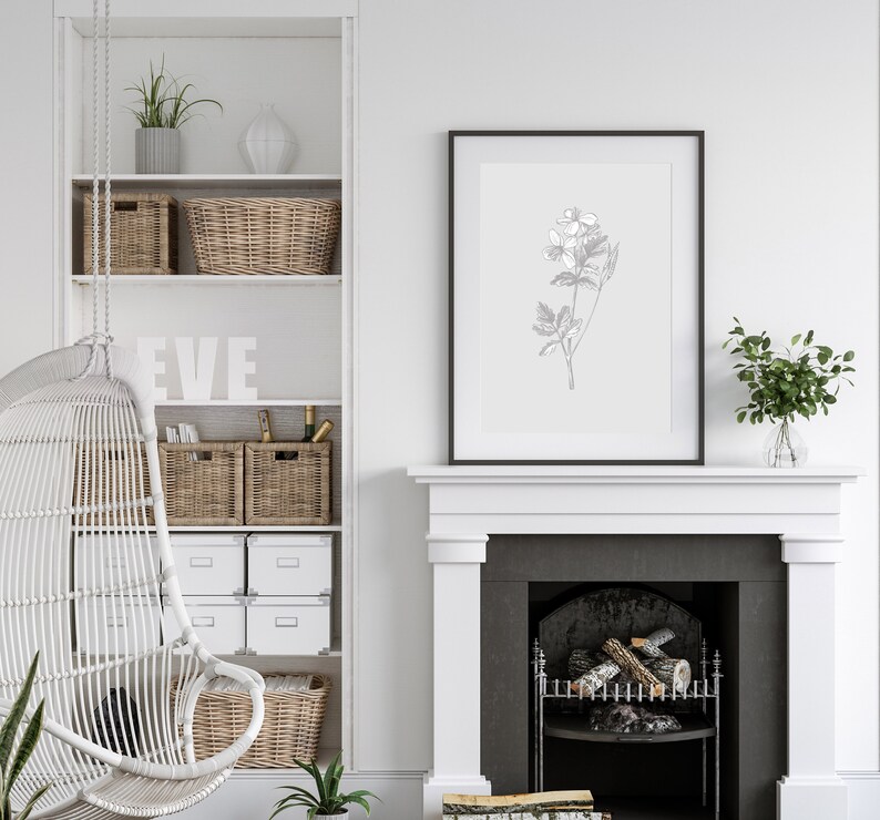 May include: A white wicker hanging chair with a white fireplace and a black framed print of a botanical illustration above it. The fireplace has a black grate and logs inside.