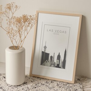 K&ouml;nnte beinhalten: Ein gerahmter Druck der Skyline von Las Vegas in Schwarzwei&szlig;. Der Druck ist in einem hellen Holzrahmen und liegt auf einem wei&szlig;en Teppich. Der Text "Las Vegas, Nevada" ist oben auf dem Druck gedruckt.
