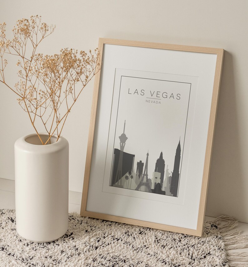 K&ouml;nnte beinhalten: Ein gerahmter Druck der Skyline von Las Vegas in Schwarzwei&szlig;. Der Druck ist in einem hellen Holzrahmen und liegt auf einem wei&szlig;en Teppich. Der Text "Las Vegas, Nevada" ist oben auf dem Druck gedruckt.