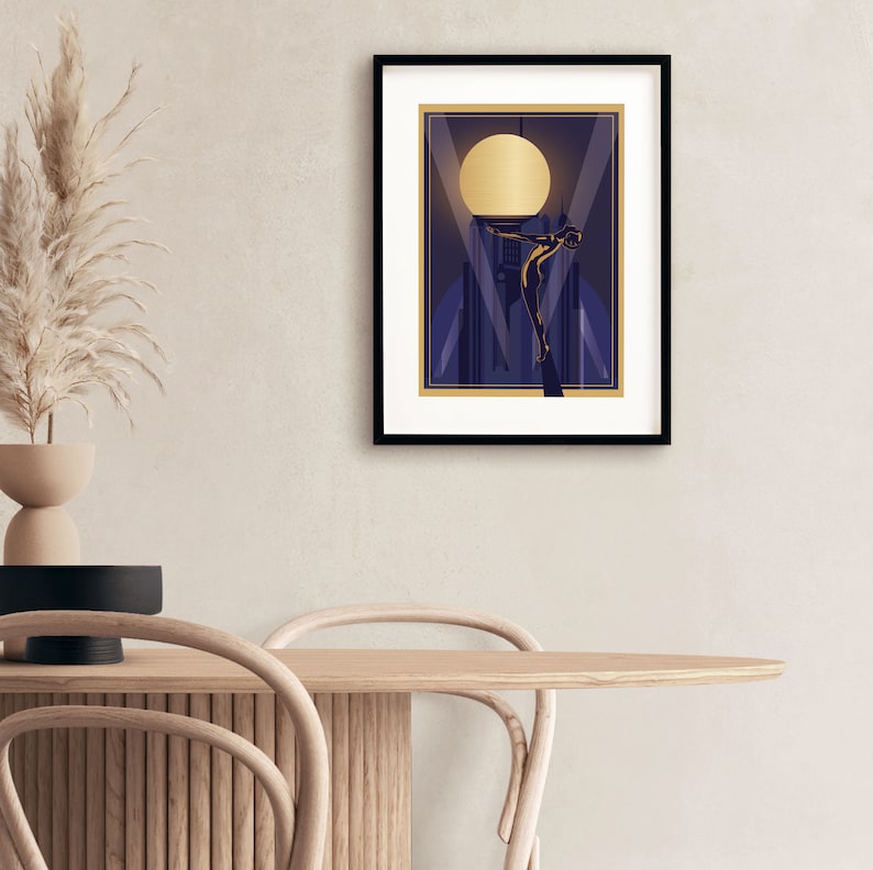 May include: A framed print of a stylized illustration of a woman standing on a building with a large golden moon in the background. The illustration is in a dark blue color scheme with gold accents.