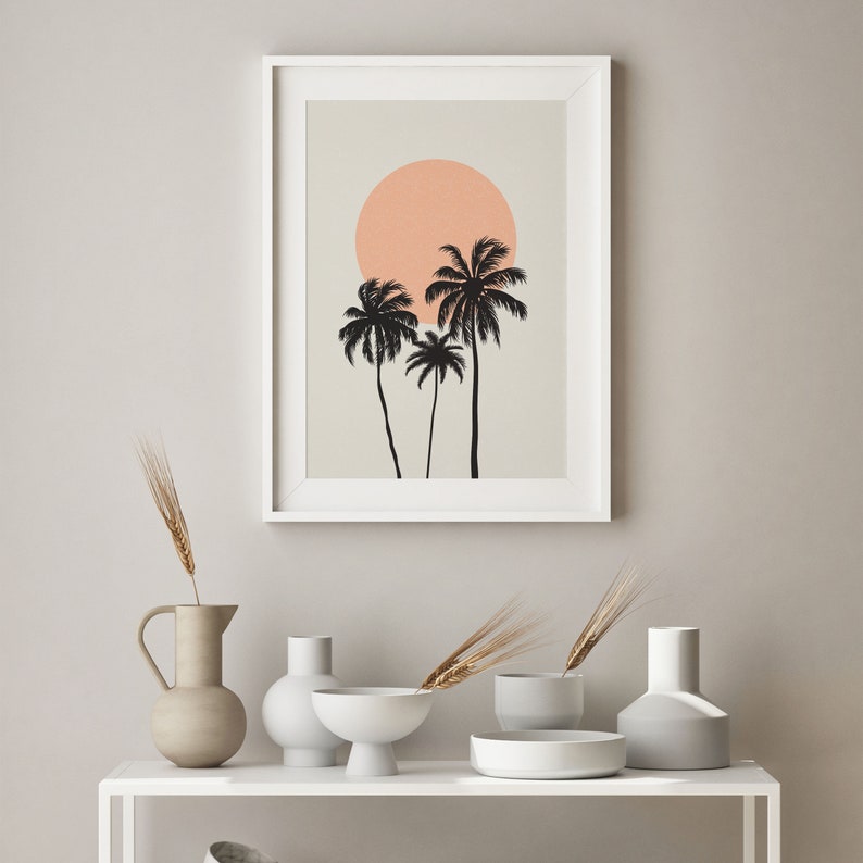May include: A white framed print with a minimalist design of three palm trees and a peach colored sun on a beige background.