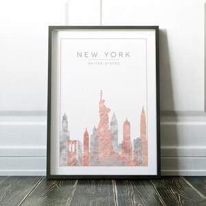 May include: A framed print with a watercolor illustration of the New York City skyline in shades of pink and gray. The print includes the Statue of Liberty and the text "NEW YORK, UNITED STATES".