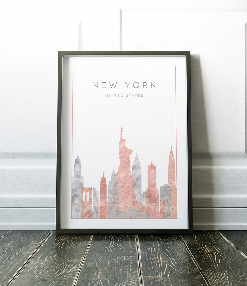 May include: A framed print with a watercolor illustration of the New York City skyline in shades of pink and gray. The print includes the Statue of Liberty and the text "NEW YORK, UNITED STATES".