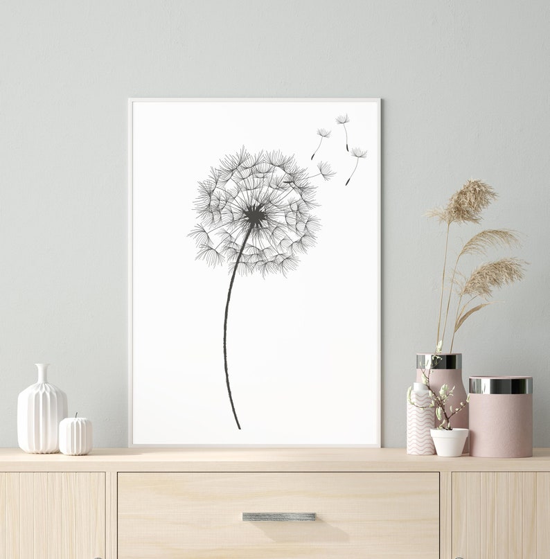 May include: A black and white illustration of a dandelion with seeds blowing in the wind. The dandelion is in the centre of a white frame, which is hanging on a light grey wall.