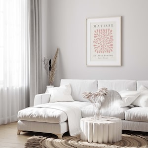 May include: A white sectional sofa with a white throw blanket and a white coffee table with a unique design. A framed art print with the text "MATISSE GALERIE BOHEME Papiers Decoupes" hangs on the wall behind the sofa.