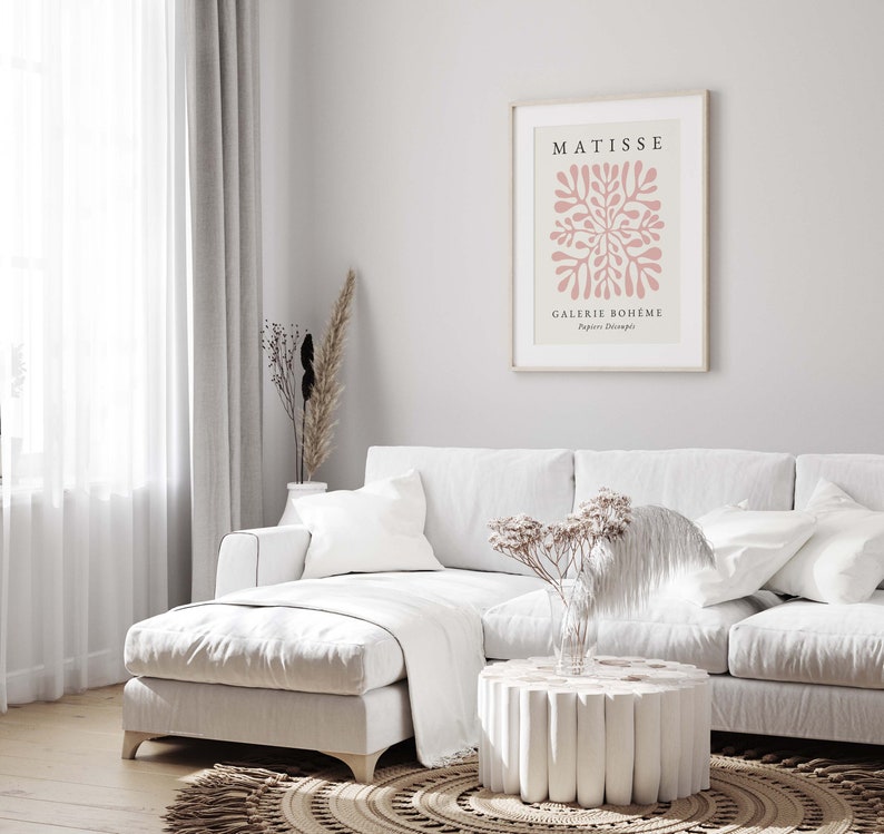 May include: A white sectional sofa with a white throw blanket and a white coffee table with a unique design. A framed art print with the text "MATISSE GALERIE BOHEME Papiers Decoupes" hangs on the wall behind the sofa.
