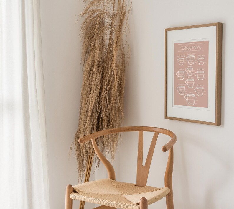 May include: A framed print with a pink background and white text that reads "Coffee Menu" with illustrations of coffee cups. The print is hanging on a white wall next to a wooden chair with a woven seat.