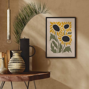 May include: A framed print of three stylized sunflowers in yellow and green on a cream background. The sunflowers have black centers and are arranged in a cluster.