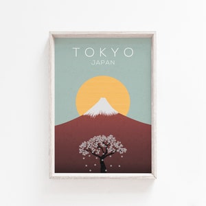 Puede incluir: Una impresi&oacute;n enmarcada con un dise&ntilde;o minimalista que presenta una imagen estilizada del Monte Fuji, un &aacute;rbol de cerezo en flor y un sol amarillo sobre un fondo azul y marr&oacute;n. El texto "TOKYO JAP&Oacute;N" est&aacute; impreso en la parte superior de la impresi&oacute;n.