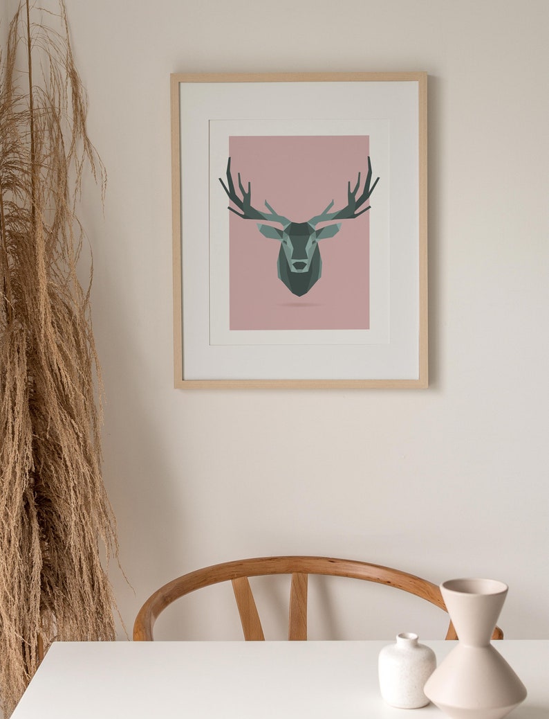 May include: A framed print of a geometric deer head illustration on a pink background. The deer is a dark green color with antlers.