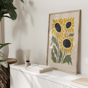 May include: A framed print of a stylized illustration of three sunflowers with yellow petals and black centers on a cream background.