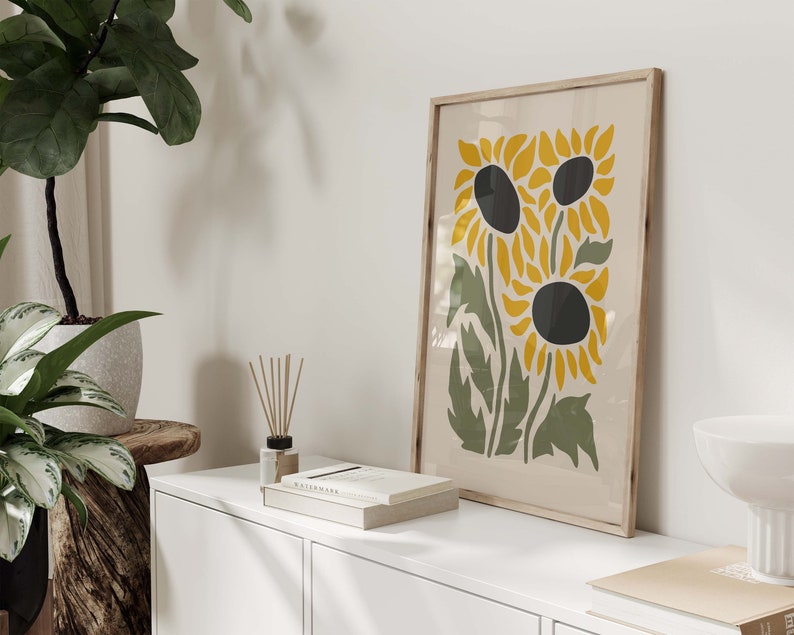May include: A framed print of a stylized illustration of three sunflowers with yellow petals and black centers on a cream background.