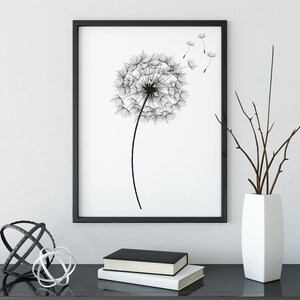 May include: Black and white framed print of a dandelion with seeds blowing in the wind, displayed on a black table with a white vase and brown branches, and two metal orbs.