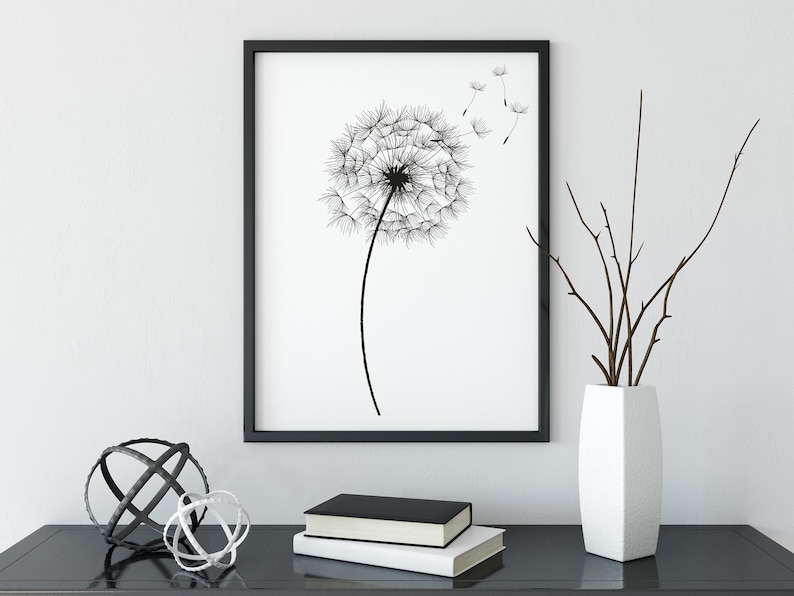 May include: Black and white framed print of a dandelion with seeds blowing in the wind, displayed on a black table with a white vase and brown branches, and two metal orbs.